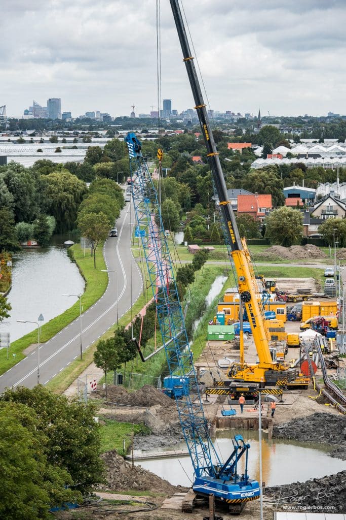 Overzichtsfoto van het plaatsen van een zinker met grote hijskraan. In de verte ligt Den Haag.