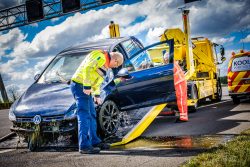 Inspecteur Rijkswaterstaat kijkt naar een auto die te water was geraakt en nu op een bergingswagen wordt geladen.