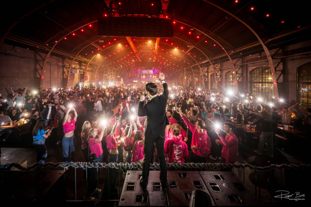 De eventfotograaf achter de zanger met de zaal voor zich, tijdens de Bier Cantus in de Koepelhal in Tilburg