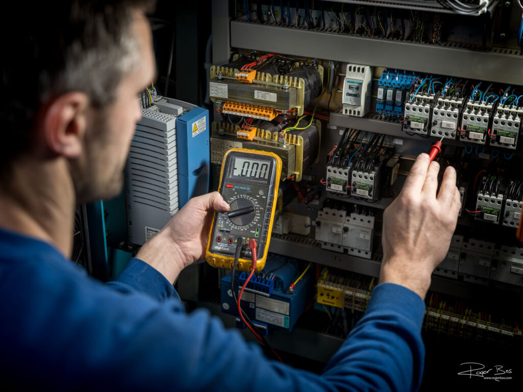 Electrotechnicus aan het werk in een schakelkast met een spanningsmeter. Fotograaf voor industrie en zakelijke markt.