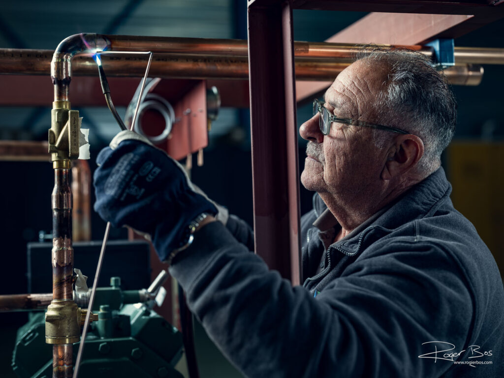 Portret van oudere installateur die een koelinstallatie soldeert. Foto door portretfotograaf Rogier Bos, genomen in Ridderkerk.