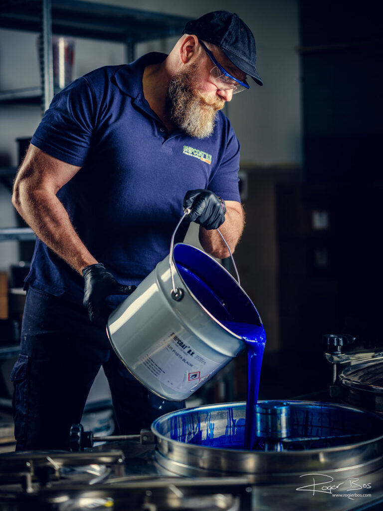 Medewerker van een bedrijf gespecialiseerd in bijzondere coatings giet blauwe verf in een verfmengmachine. Industrieel portret door fotograaf gespecialiseerd in industriele fotografie.