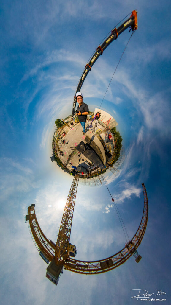 Tiny world portret van industrieel fotograaf boven op een bouwproject met hijskranen in de achtergrond.
