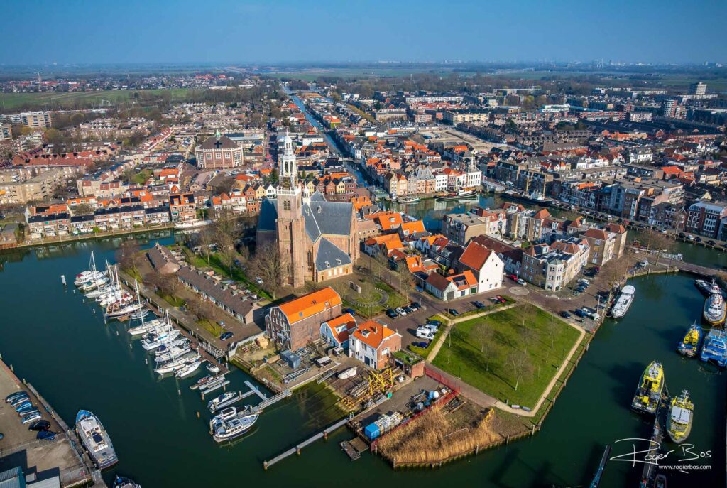 Dronefoto van Maassluis met een kerk die op een eiland ligt, omringd door water en historische bebouwing