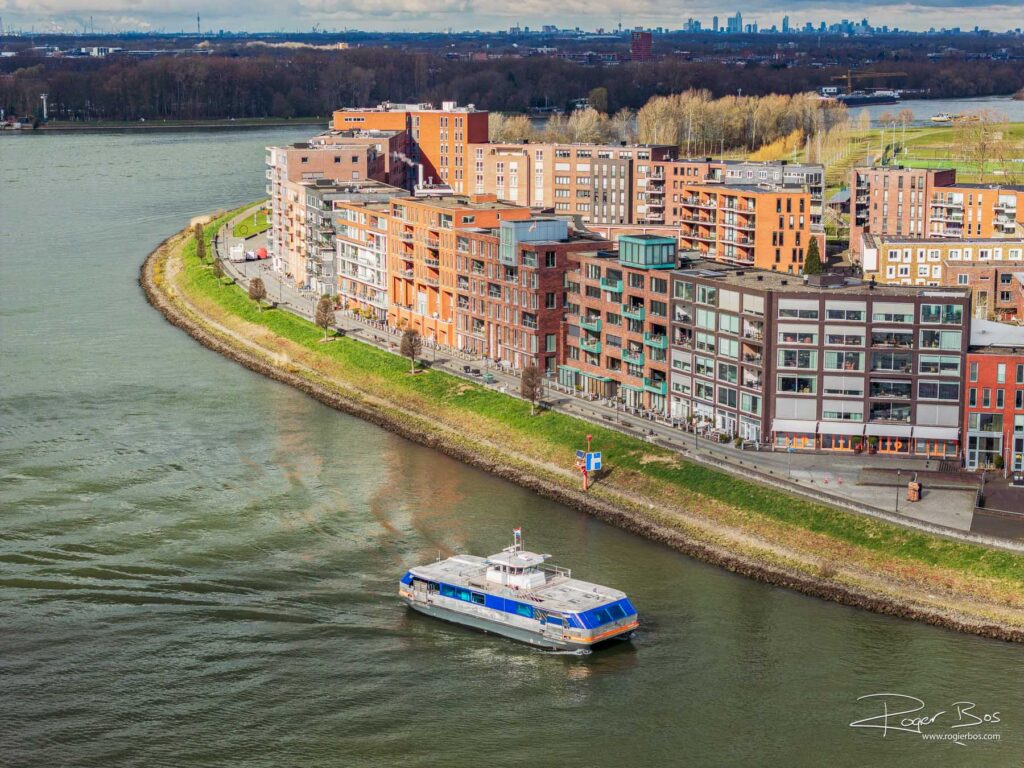Dronefoto van Papendrecht waar een pont aanmeert bij het Merwehoofd, met uitzicht op de rivier en moderne appartementen