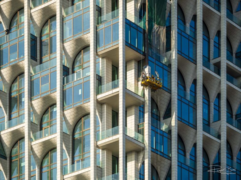 Spectaculaire bouwfotografie van een moderne woontoren in aanbouw, met bouwvakkers aan de gevel — vastgelegd door fotograaf Rogier Bos.