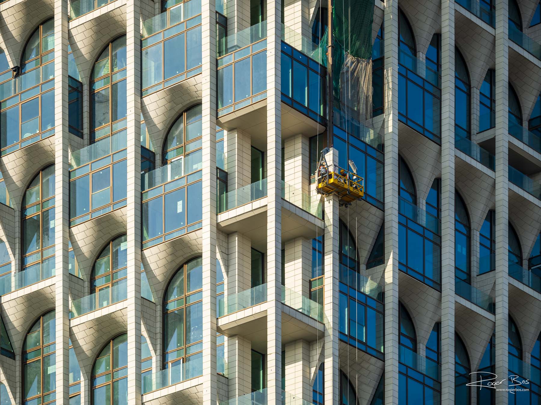 Spectaculaire bouwfotografie van een moderne woontoren in aanbouw, met bouwvakkers aan de gevel — vastgelegd door fotograaf Rogier Bos.