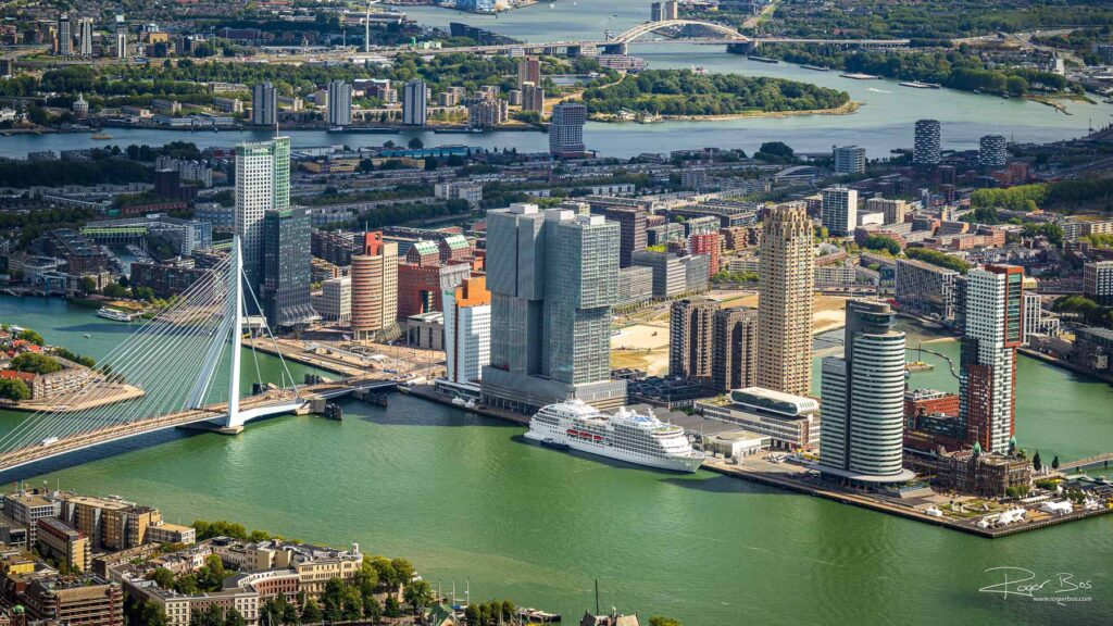 Aerial photo of Rotterdam’s Kop van Zuid with the Erasmus Bridge, De Rotterdam towers, Wilhelminapier and a docked cruise ship.