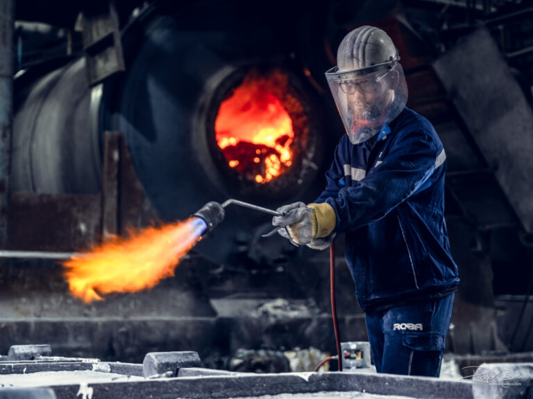 Industriële fotograaf legt operator vast met gasbrander in aluminiumfabriek bij hoge temperaturen.