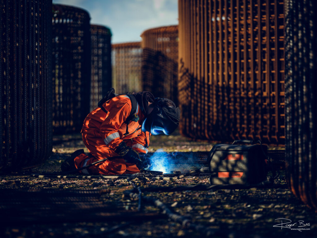 Industriële fotograaf legt lasser vast tussen vlechtwerkkorven tijdens constructiewerk voor betonnen brugdelen.