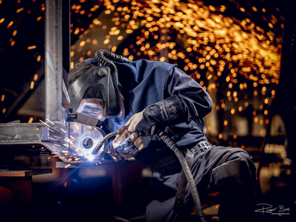 Industriële fotograaf legt lasser vast die werkt aan stalen onderdelen van een waterkering.