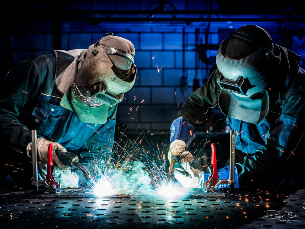 Industriële fotograaf legt twee lassers vast die gelijktijdig werken aan staalconstructie, vastgelegd in hoge resolutie.