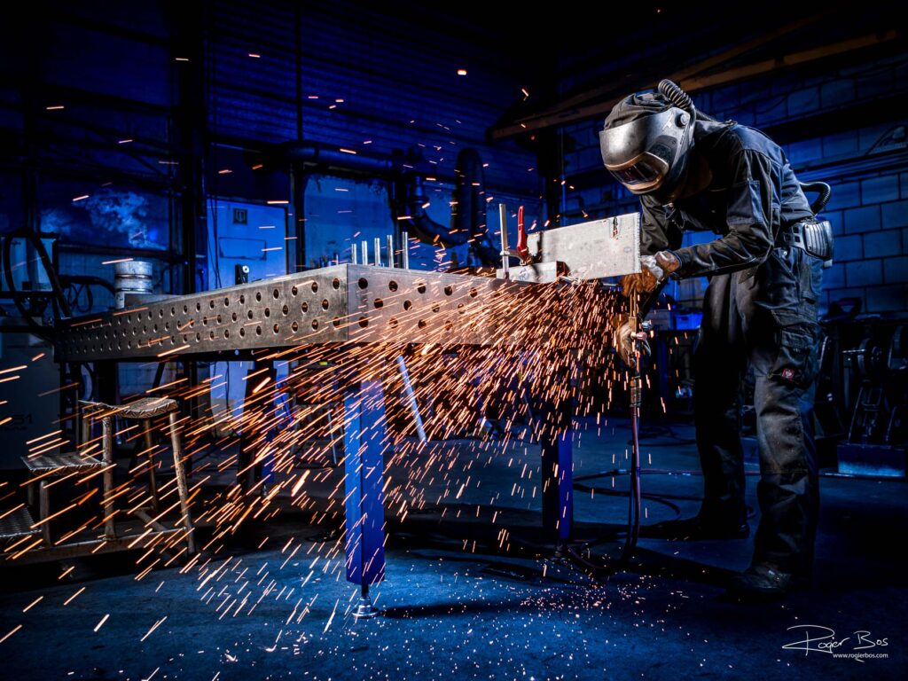 Industriële fotograaf legt metaalbewerker vast die met snijbrander werkt in staalwerkplaats, gefotografeerd in hoge resolutie.