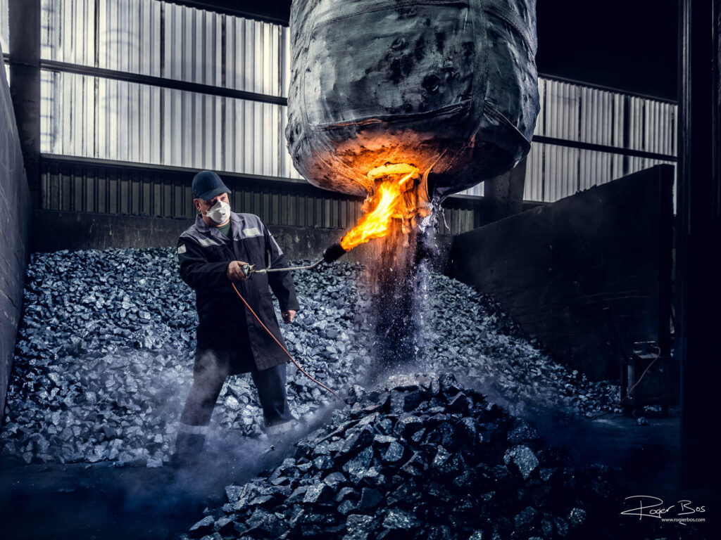 Industriële fotograaf legt operator vast die big bag met silicium openbrandt in fabriekshal in Delfzijl.