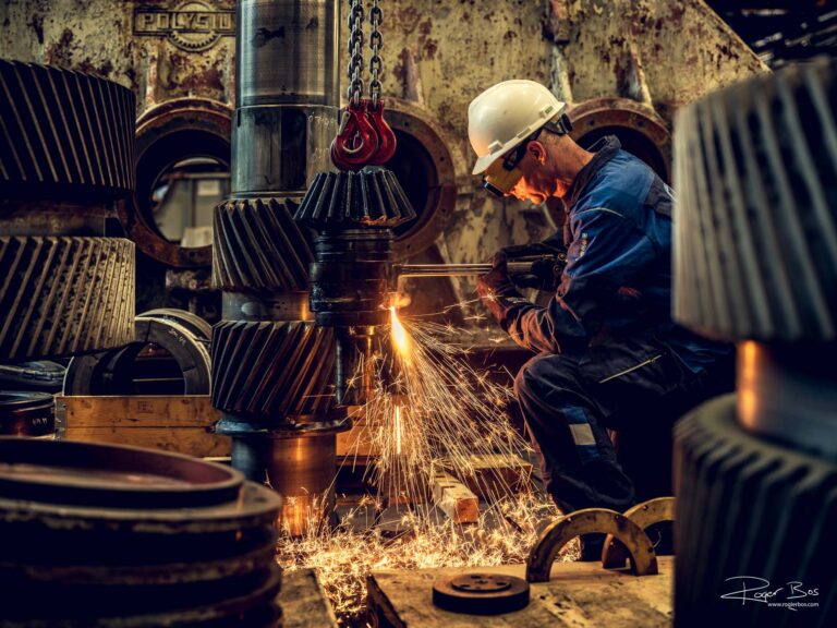 Industriële fotograaf legt lasser vast met snijbrander bij GBS International, werk aan zware tandwielen in warme lichtomstandigheden.