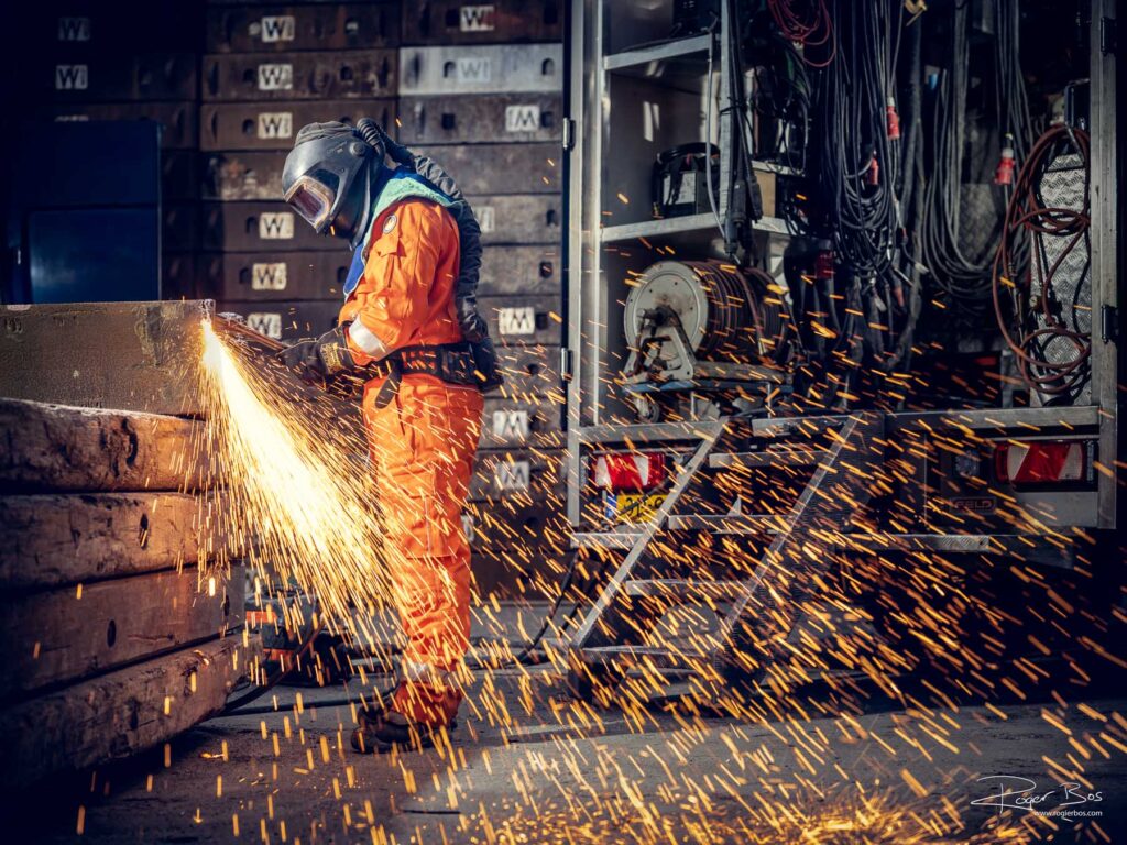 Industriële fotograaf legt branderwerker vast die stalen onderdelen doorsnijdt met snijbrander op industriële locatie.
