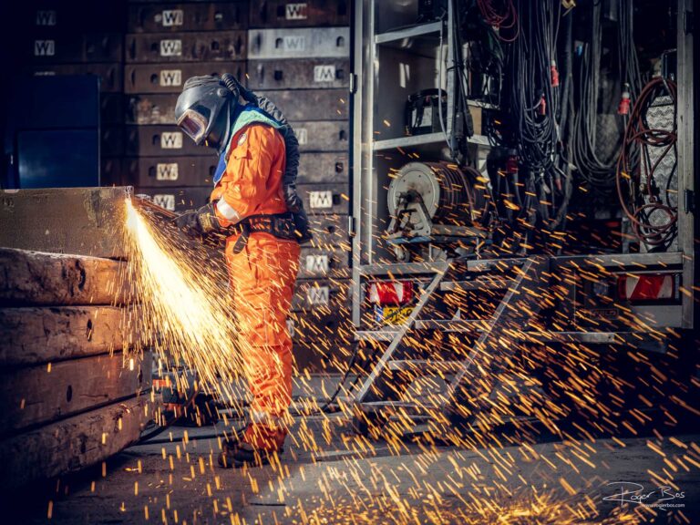 Industriële fotograaf legt branderwerker vast die stalen onderdelen doorsnijdt met snijbrander op industriële locatie.