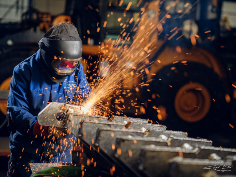 Industriële fotograaf legt metaalbewerker vast die met snijbrander werkt aan stalen constructie.