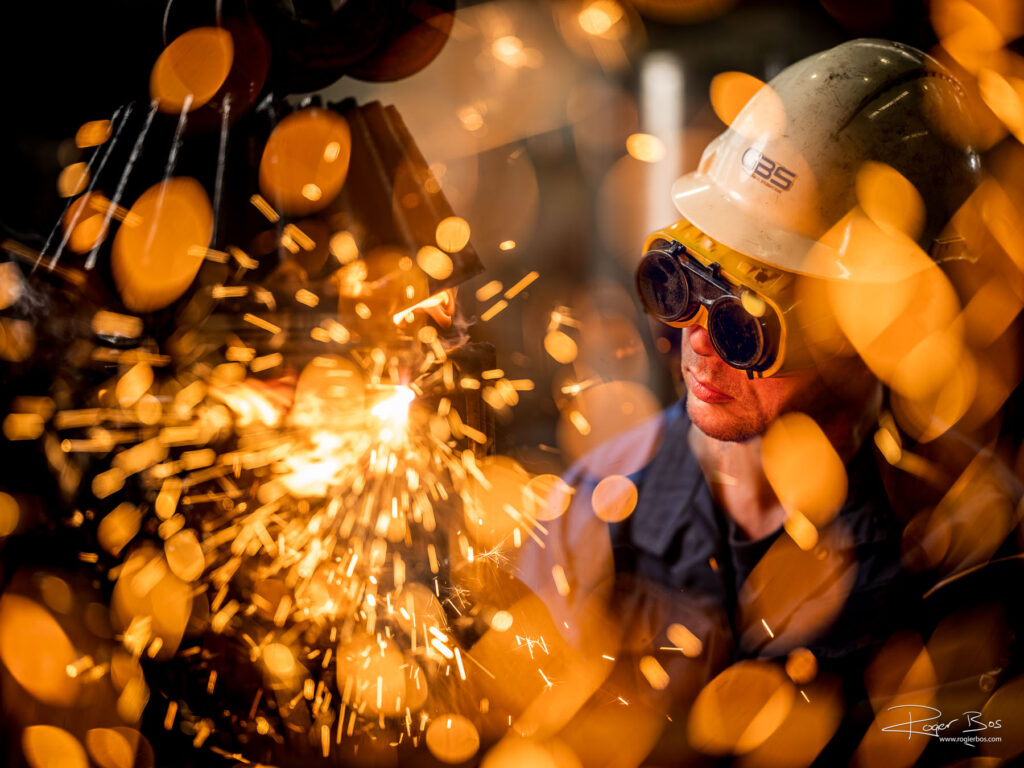 Industriële fotograaf legt vakman met snijbrander vast tussen vonkenregen, dichtbij en vol focus.