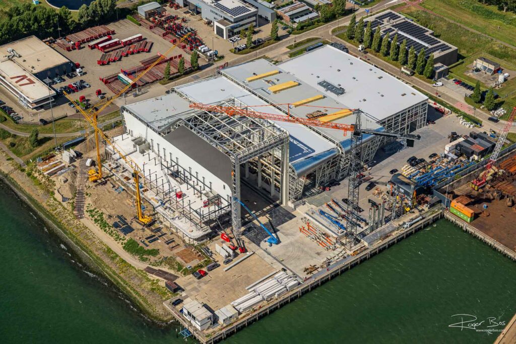 Luchtfoto van een bouwproject aan de kade in Vlaardingen met grote hal in aanbouw, kranen en kadeconstructie.