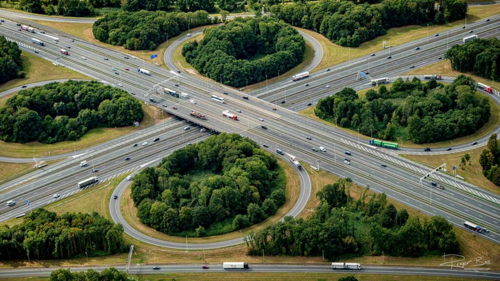 Luchtfoto van knooppunt Hoevelaken bij Amersfoort, waar de A1 en A28 elkaar kruisen met klaverbladlussen en druk verkeer.