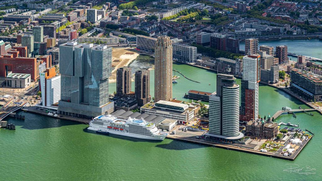 Luchtfoto van de Wilhelminapier in Rotterdam met De Rotterdam, New Orleans, Montevideo, Hotel New York en een aangemeerd cruiseschip.