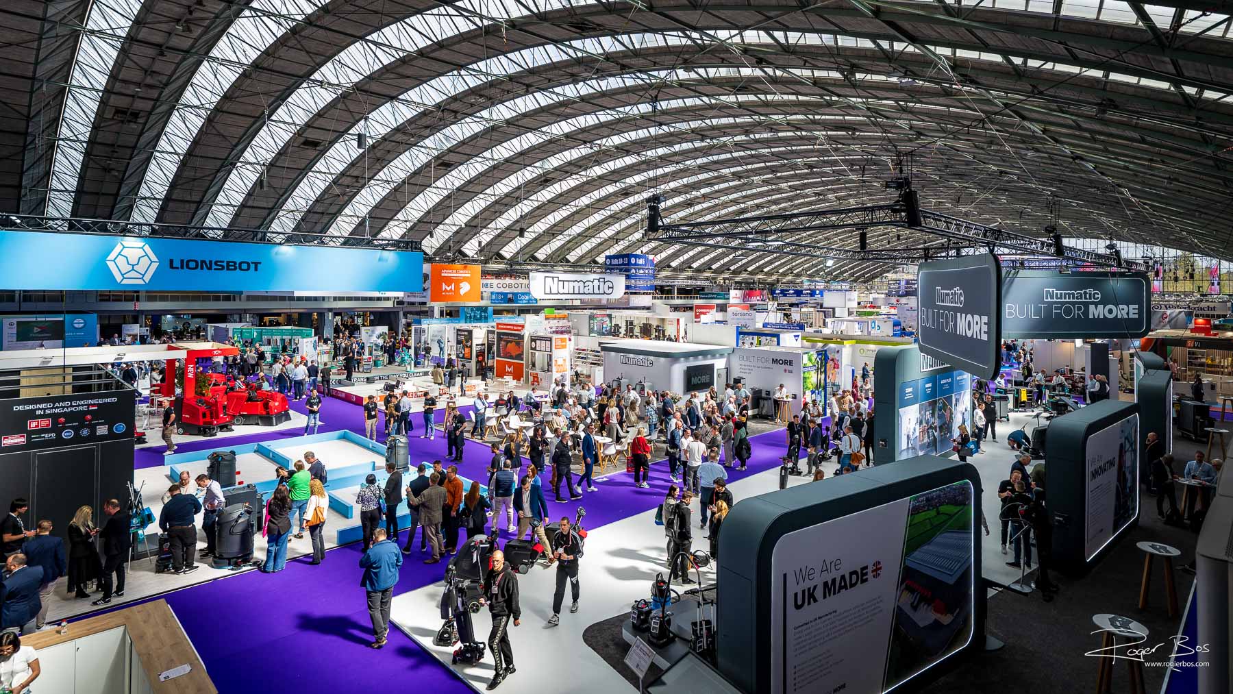 Overzichtsfoto van de drukbezochte Interclean-beurs in de RAI Amsterdam, met stands van Lionsbot en Numatic onder het kenmerkende gewelfde dak.
