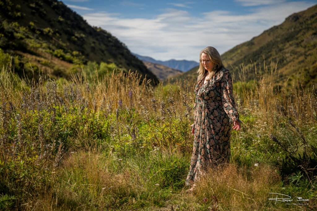 Woman in a floral dress walking through wild lupins and tall grass in a New Zealand mountain valley.