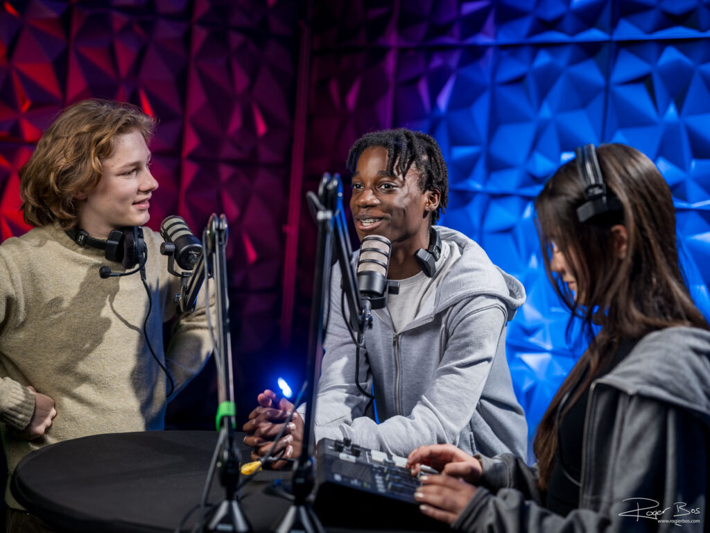 Drie studenten nemen podcast op in professionele podcaststudio met Røde-microfoons en akoestische wanden