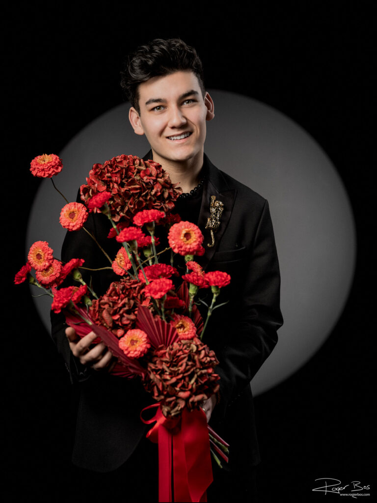 Personal branding portret van een jonge bloemenstylist in zwart pak met een rood boeket hydrangea's en anjers in een fotostudio in Rotterdam
