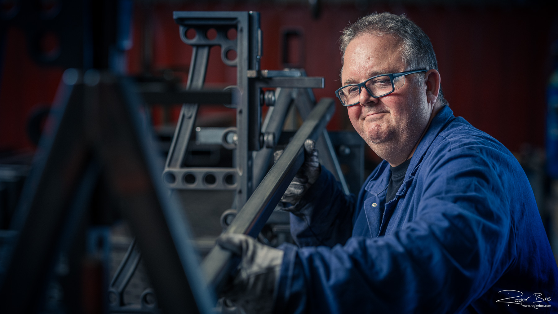 Monteur in blauwe werkkleding werkt aan een stalen constructie in een industriële werkplaats.